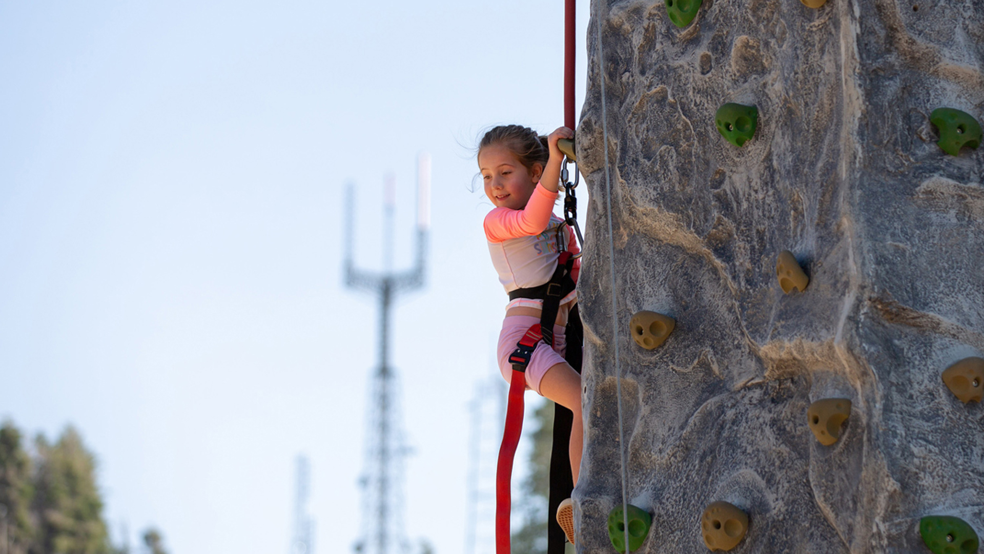 Young Girl Climbing The Stack Rock Climbing Wall With Deer Point Towers In The Background In The Explorer Base Camp Summer 2021 At Bogus Basin Mountain Recreation Area Photo By Luke Tokunaga 1920px1080px