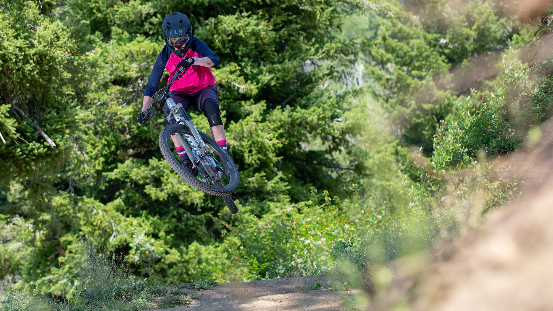 Female Mountain Biker In Pink And Black Jersey Going Over Jump In Mid Air On The Basin Gravity Park Bike Park Trail Summer At Bogus Basin Mountain Recreation Area 1920px1080px