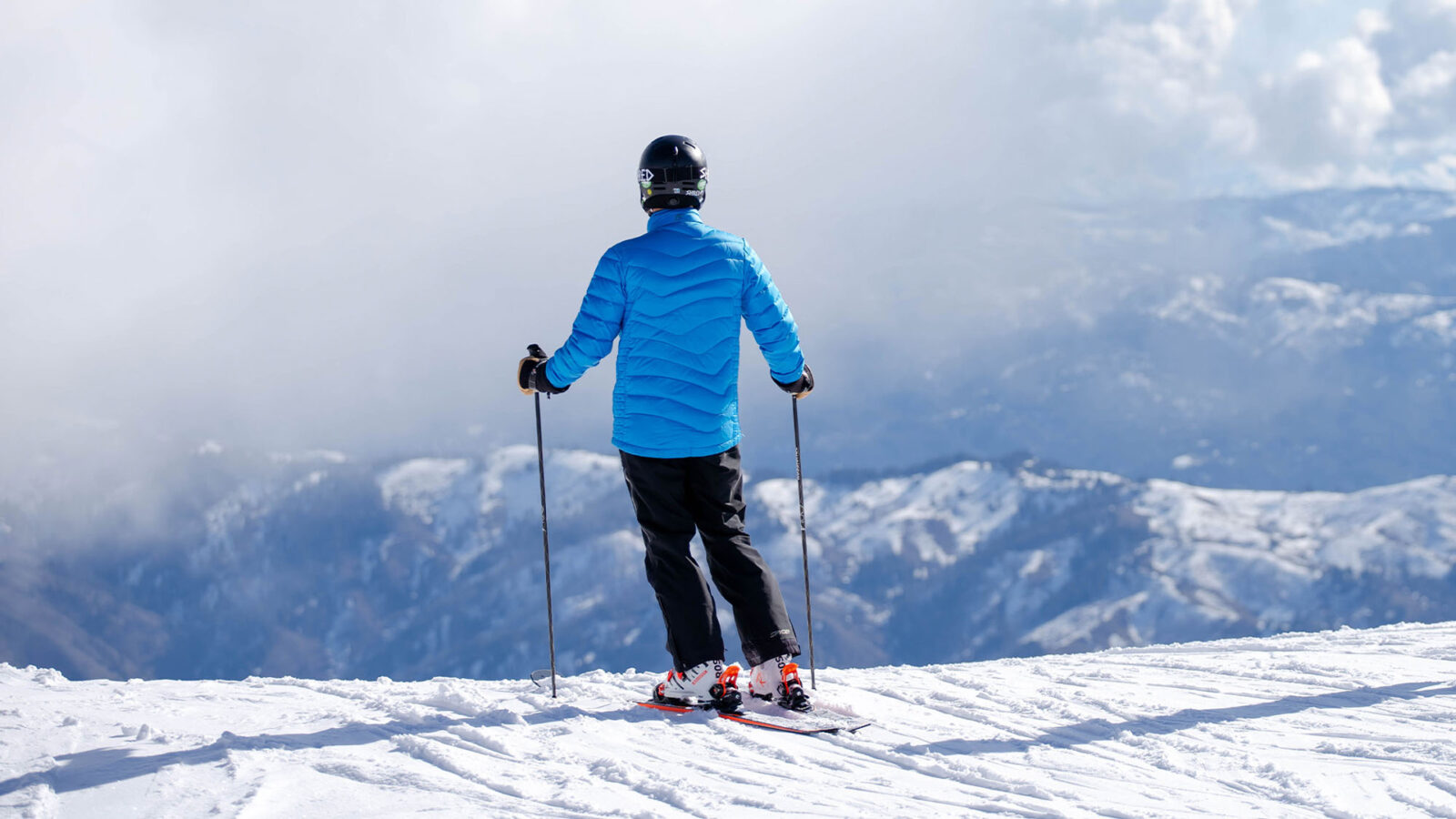 Male Skier With Bright Blue Puffer Jacket Standing On Edge Of Hill Looking Out Into The Distance With Snowy Mountains And Fog In The Background Winter At Bogus Basin Mountain Recreation Area 1920px1080px