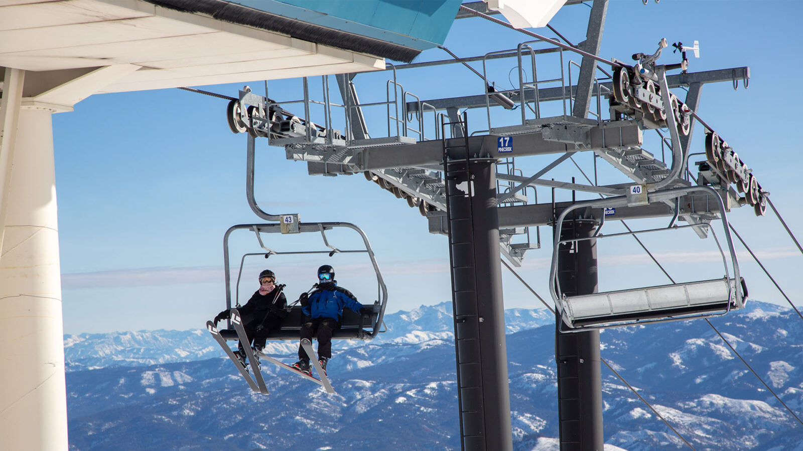 Two Skiers About To Get Off Pine Creek Chairlift With Mountain Range In Background On A Bluebird Day Winter At Bogus Basin Mountain Recreation Area 1920px1080px