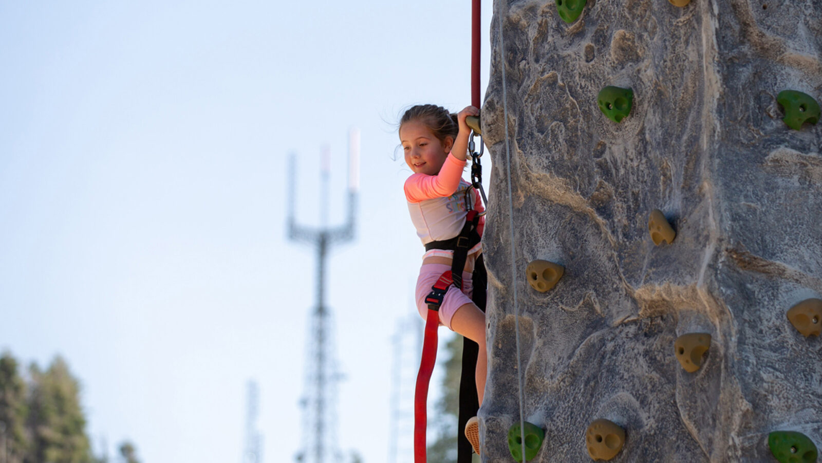 Female Child Climbing The Stack Rock Climbing Wall In The Explorer Base Camp With Deer Point Towers Blurry In The Background Summer 2021 At Bogus Basin Mountain Recreation Area Photo By Luke Tokunaga 1920px1080px
